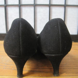 Op de afbeelding: Een paar zwarte su&egrave;de pumps met een lage, afgeronde hak. De schoenen hebben een klassiek ontwerp, met een spitse neus en een gladde afwerking. De hakken zijn ongeveer 5 cm hoog.