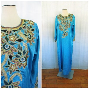 May include: A long, turquoise blue dress with intricate gold and silver embroidery featuring floral designs. The dress has long sleeves and a round neckline.