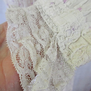 May include: Close-up of a white lace trim with a delicate floral pattern. The lace is ruffled and has a soft, vintage look.