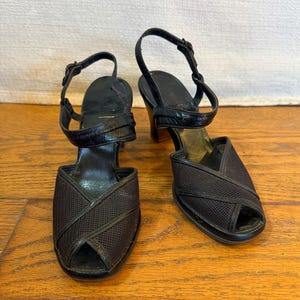 Op de afbeelding: Een paar zwarte peep-toe slingback hakken met een bovenwerk van gestructureerde mesh-stof met kruislingse details, een enkelbandje met gesp en een effen zwarte hak. Het voetbed aan de binnenzijde is zwart met een gladde afwerking.