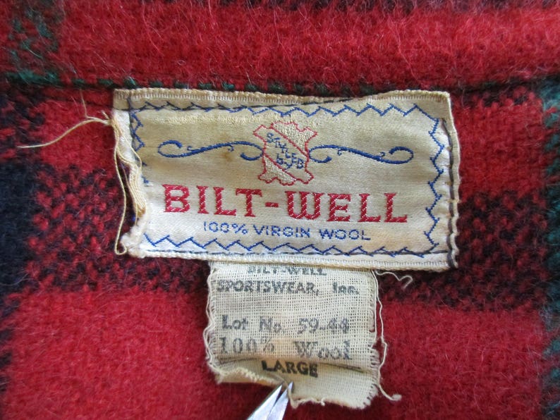 May include: A red and black plaid wool shirt with a white label that reads "BILT-WELL 100% VIRGIN WOOL". The label also includes the text "SPORTSWEAR, Inc. Lot No. 59-44 100% Wool LARGE".