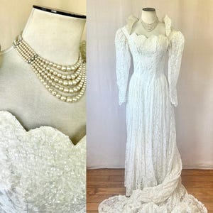 May include: A vintage white lace wedding dress with long sleeves and a flowing skirt. The dress features a scalloped neckline and a long train. A multi-strand pearl necklace is displayed on a mannequin.