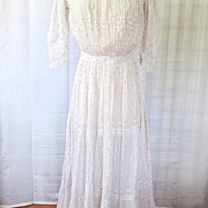 May include: A white cotton dress with a high neck and a gathered skirt. The dress has a small purple polka dot pattern and is decorated with lace trim.