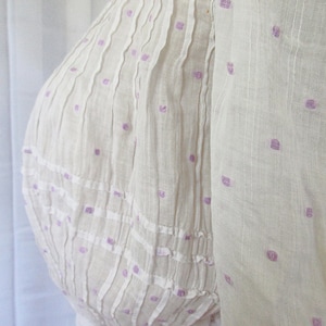 May include: White cotton dress with a purple polka dot pattern. The dress has a gathered bodice and a full skirt.