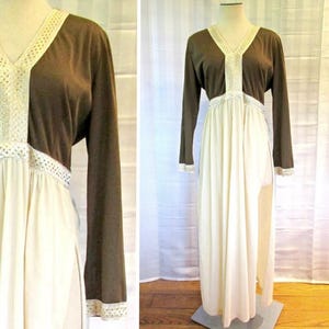 May include: A vintage maxi dress with a brown bodice and long sleeves, featuring a V-neck. The cream-coloured skirt is complemented by white lace trim on the neckline, waist, and cuffs. The dress is displayed on a mannequin, showcasing its retro design.