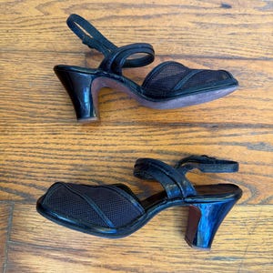 Op de afbeelding: Een paar zwarte slingback-sandalen met een neus van mesh-stof, een gladde band over de wreef, een verstelbare enkelband met gesp en een uitlopende hak van gemiddelde hoogte met een glanzende afwerking aan de buitenzijde.