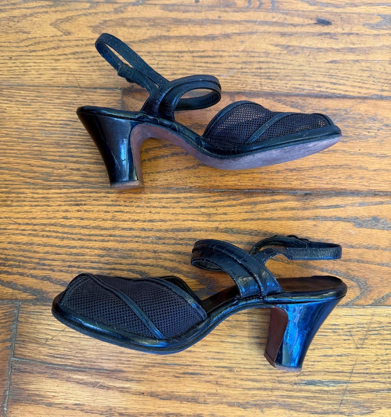 Op de afbeelding: Een paar zwarte slingback-sandalen met een neus van mesh-stof, een gladde band over de wreef, een verstelbare enkelband met gesp en een uitlopende hak van gemiddelde hoogte met een glanzende afwerking aan de buitenzijde.