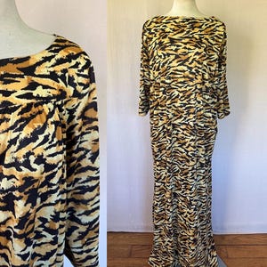 May include: A long-sleeved maxi dress with a tiger stripe pattern in shades of black, tan, and brown. The dress has a boat neckline and a flowing silhouette. The fabric appears to be lightweight and suitable for warmer weather.