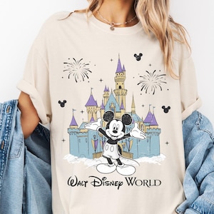 Op de afbeelding: Ivoor kleurig T-shirt met een afbeelding van Mickey Mouse voor het kasteel van Assepoester in Walt Disney World. Het ontwerp bevat vuurwerk en de tekst "Walt Disney World". Het shirt is gelabeld "Comfort Ivory".