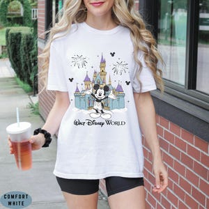 Op de afbeelding: Wit T-shirt met een kleurrijke afbeelding van Mickey Mouse voor het kasteel van Assepoester, vuurwerk en de tekst "Walt Disney World". Het shirt is gemaakt van Comfort White materiaal.