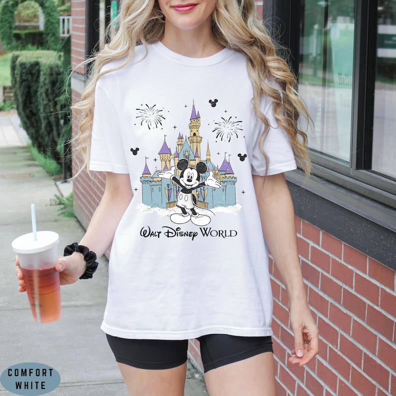 Op de afbeelding: Wit T-shirt met een kleurrijke afbeelding van Mickey Mouse voor het kasteel van Assepoester, vuurwerk en de tekst "Walt Disney World". Het shirt is gemaakt van Comfort White materiaal.