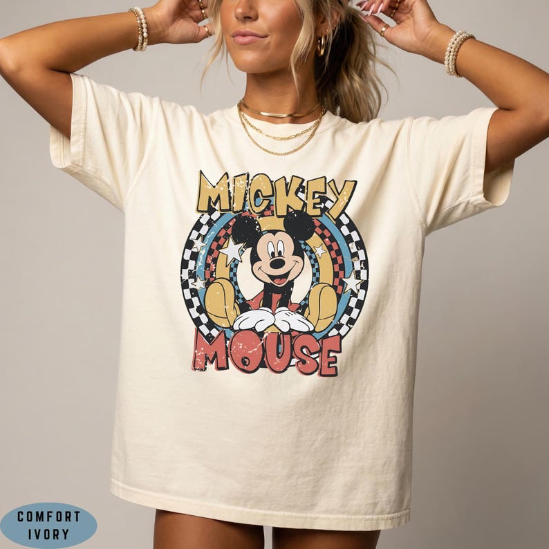 Puede incluir: Una camiseta de color marfil con un gr&aacute;fico de Mickey Mouse centrado en un marco circular. El dise&ntilde;o incluye un borde a cuadros, estrellas y el texto MICKEY MOUSE en letras negritas y desgastadas. La camiseta est&aacute; etiquetada como Comfort Ivory.