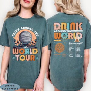 May include: Teal Comfort Blue Spruce t-shirt with a colorful graphic. The front features the text "DRINK AROUND THE WORLD TOUR 2026" with a globe design. The back has "DRINK AROUND THE WORLD" and a list of countries.