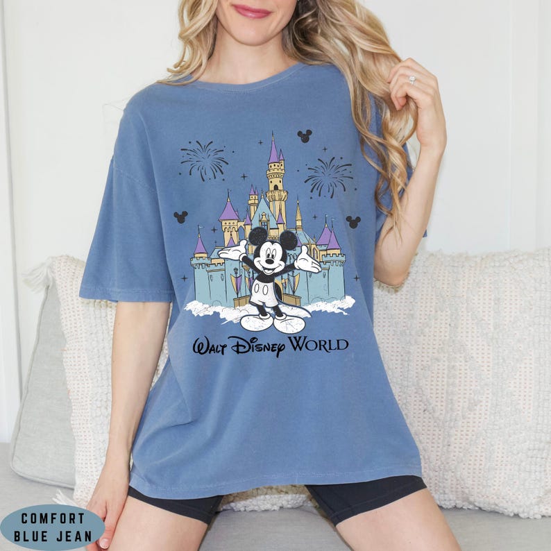 Op de afbeelding: Comfort blauw spijkerbroek t-shirt met een afbeelding van Mickey Mouse voor het kasteel van Assepoester in Walt Disney World. Het ontwerp bevat vuurwerk en Mickey Mouse silhouetten. De tekst "Walt Disney World" staat eronder.