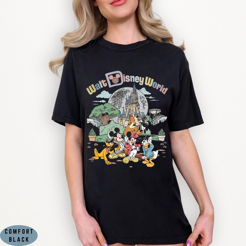 May include: Black t-shirt featuring a colorful graphic of Disney characters, including Mickey Mouse, Minnie Mouse, Donald Duck, and Goofy, in front of a castle and the words "Walt Disney World". The shirt has a crew neck and short sleeves.
