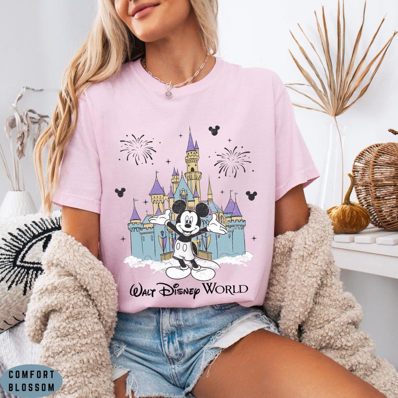 Op de afbeelding: Lichtroze T-shirt met een afbeelding van Mickey Mouse voor het kasteel van Assepoester in Walt Disney World. Het ontwerp bevat vuurwerk en de tekst "Walt Disney World".