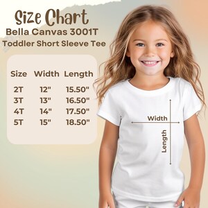 Op de afbeelding: Een jong meisje draagt een wit T-shirt met korte mouwen voor peuters. De afbeelding bevat een maattabel voor Bella Canvas 3001T shirts, met afmetingen in inches voor maten 2T tot 5T. De tabel toont breedte- en lengtematen.