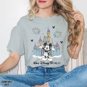 Op de afbeelding: Lichtblauw T-shirt met een afbeelding van Mickey Mouse voor het kasteel van Assepoester, vuurwerk en de tekst "Walt Disney World". Het shirt heeft een relaxte pasvorm.