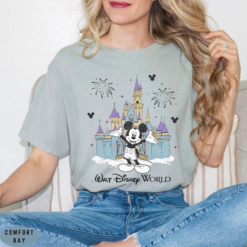 Op de afbeelding: Lichtblauw T-shirt met een afbeelding van Mickey Mouse voor het kasteel van Assepoester, vuurwerk en de tekst "Walt Disney World". Het shirt heeft een relaxte pasvorm.