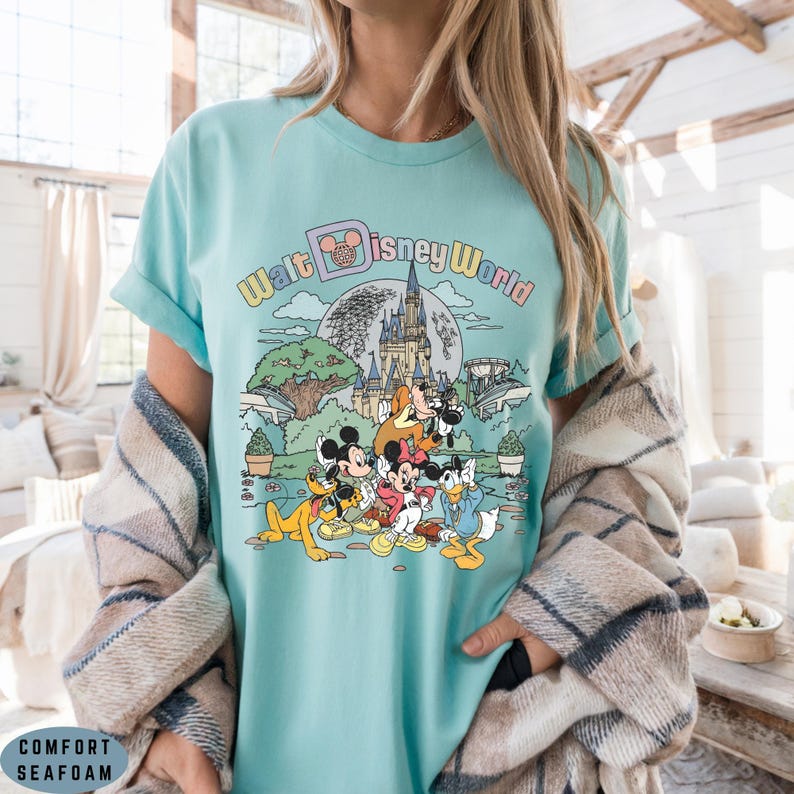 May include: Seafoam green t-shirt featuring a colorful graphic of Disney characters and the text "Walt Disney World." The design includes Mickey Mouse, Minnie Mouse, Donald Duck, and Pluto in front of a castle and a full moon.