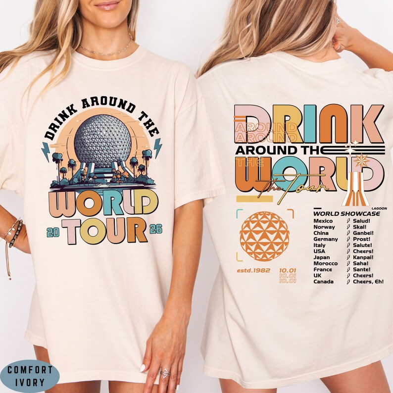 May include: Ivory-colored t-shirt with a colorful graphic design. The front features the text "DRINK AROUND THE WORLD TOUR 26" with a graphic of a sphere and trees. The back has "DRINK AROUND THE WORLD" and a list of countries.