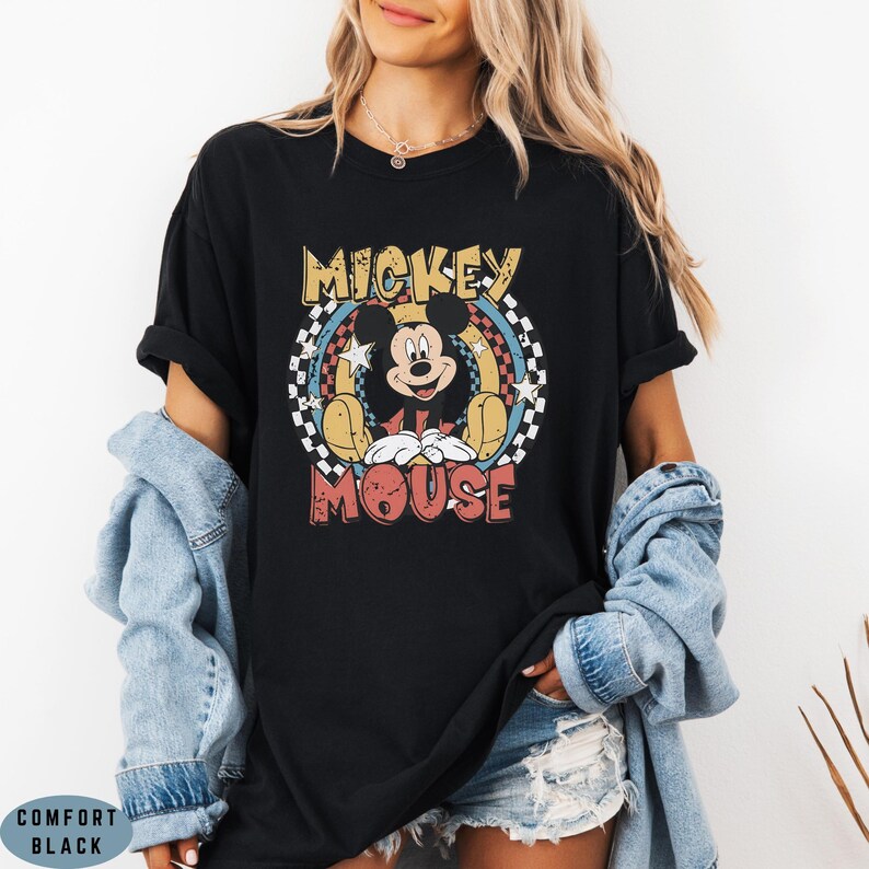 Puede incluir: Una camiseta negra de manga corta con un gr&aacute;fico de Mickey Mouse centrado en un dise&ntilde;o circular. El gr&aacute;fico incluye el texto MICKEY MOUSE en letras negritas, rodeado por un patr&oacute;n de cuadros, estrellas y detalles en amarillo y azul.