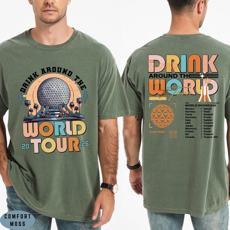 May include: Olive green t-shirt with a graphic design. The front features the text "DRINK AROUND THE WORLD TOUR 20 26" with a colorful illustration. The back has "DRINK AROUND THE WORLD" and a list of countries.
