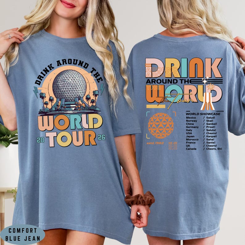 May include: Comfort blue jean t-shirt with a colorful graphic. The front features the text "DRINK AROUND THE WORLD TOUR 26" with a globe design. The back has "DRINK AROUND THE WORLD" and a list of countries.