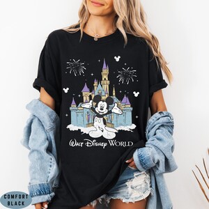 Op de afbeelding: Zwart T-shirt met een afbeelding van Mickey Mouse voor het kasteel van Assepoester in Walt Disney World. Het ontwerp bevat vuurwerk en de tekst "Walt Disney World" in het wit. Het shirt is een Comfort Black-stijl.