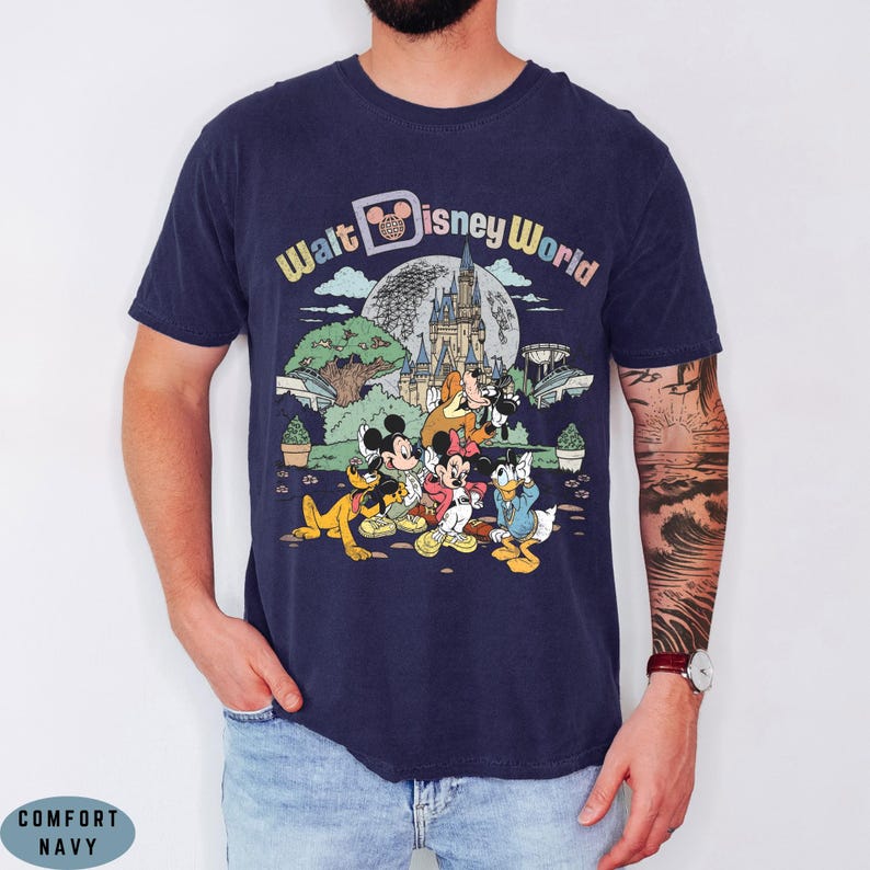 May include: Navy blue t-shirt featuring a colorful graphic of Disney characters in front of a castle, with the words "Walt Disney World" in a rainbow font. The shirt is a classic crew neck.