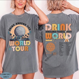 May include: Comfort grey t-shirt with a graphic design. The front features the text "DRINK AROUND THE WORLD TOUR 26" with a colorful illustration. The back of the shirt has "DRINK AROUND THE WORLD" and a list of countries.