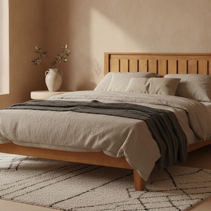 May include: A wooden bed frame with a slatted headboard, dressed in light beige bedding and a dark gray throw blanket. The bed is positioned in a room with a light-colored rug featuring a black geometric pattern and a white vase with greenery.