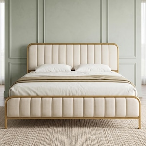 May include: A bed frame featuring a gold-toned metal structure with a rounded rectangular headboard and footboard. Both the headboard and footboard are upholstered in cream-colored fabric with vertical channel tufting. Two white pillows are placed.