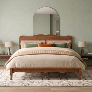 May include: A wooden bed frame with a curved headboard featuring woven cane paneling. The bed is dressed in a beige quilted comforter, two green pillows, and one orange pillow. It is positioned in front of an arched wall mirror.