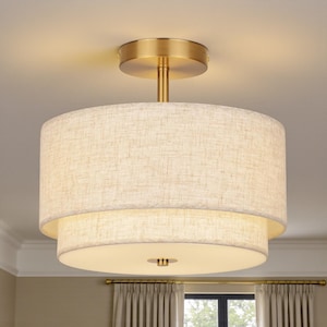 May include: A two-tiered ceiling light fixture with a brass finish and a linen shade. The top tier is a larger cylinder, and the bottom tier is a smaller, circular shape. The fixture is mounted on a brass base.