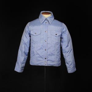 Op de afbeelding: Een lichtblauw denim jack met een knoopsluiting en twee borstzakken.