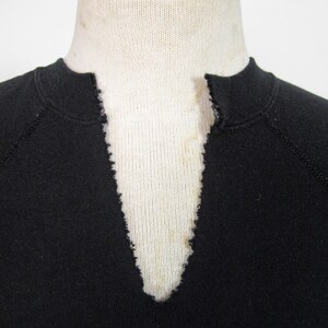 May include: Close-up of the neckline of a black sweatshirt with a V-neck. The neckline is frayed and has a light blue stain.