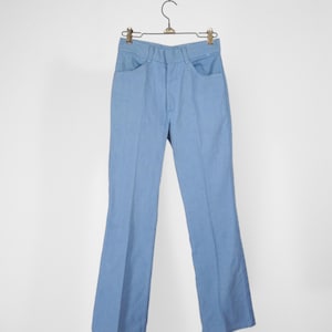 Pode incluir: Calça azul claro de boca larga pendurada em um cabide. A calça tem perna reta e abertura da perna larga.