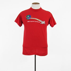 Könnte beinhalten: Rotes T-Shirt mit einer Grafik eines Raumschiffs, das einen Globus umkreist, mit dem Text "Scout is Bound...With America's Youth" und "1989 National Jamboree".