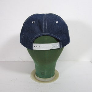 Puede incluir: Una gorra de b&eacute;isbol de mezclilla azul con una correa ajustable de pl&aacute;stico blanco. La gorra est&aacute; en una cabeza de maniqu&iacute; verde.