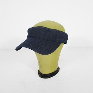 Puede incluir: Una visera de denim azul oscuro con una visera curva. La visera está en una cabeza de maniquí.