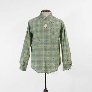 May include: A long-sleeved, button-down shirt in shades of green and white, featuring a plaid pattern with small, dark accents. The shirt has a classic collar, a chest pocket, and is displayed on a mannequin.