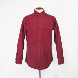 May include: A long-sleeved button-down shirt in a deep burgundy red color. The shirt has two chest pockets and a button-up collar.