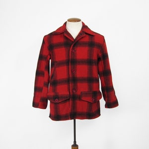 Puede incluir: Una chaqueta de lana roja y negra a cuadros con cierre de botones y dos bolsillos de solapa.