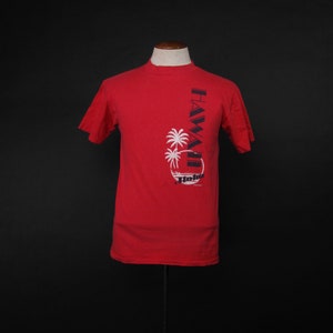 Może przedstawiać: Czerwony T-shirt z krótkim rękawem z czarno-białym nadrukiem palm i tekstem "HAWAII" i "Honolulu" z przodu.