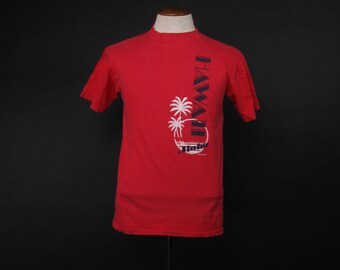 May include: Red short-sleeved t-shirt with a black and white graphic of palm trees and the text "HAWAII" and "Honolulu" on the front.