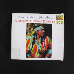May include: A white CD case with a colorful image of a Native American man in traditional clothing. The text on the case reads "Apache, Sioux, Navajo... AMERICAN INDIAN DANCES 3CD".