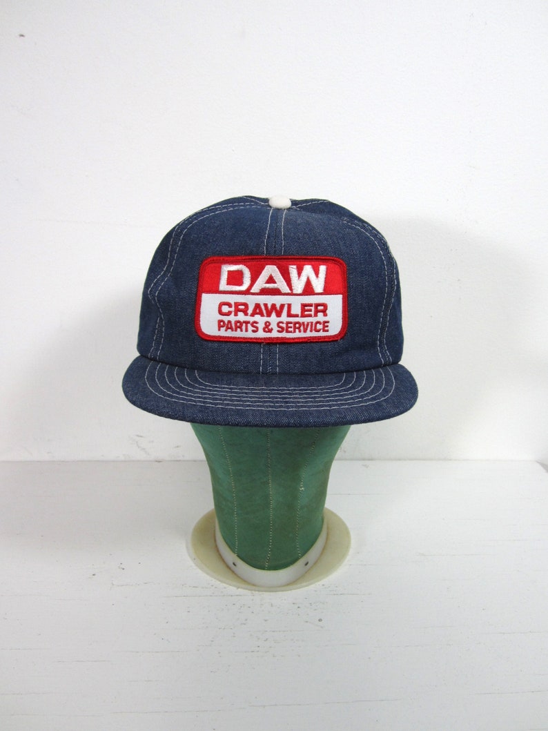Puede incluir: Un gorro de camionero de mezclilla azul con una malla blanca en la parte posterior. El gorro tiene un parche rojo y blanco que dice "DAW CRAWLER PARTS & SERVICE".
