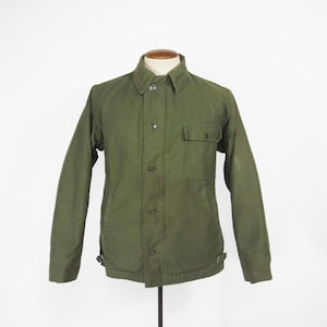 May include: Olive green jacket with a button-up front, a collared neckline, and a single chest pocket. The jacket is displayed on a mannequin and has long sleeves. The jacket is a solid color and appears to be made of a durable fabric.