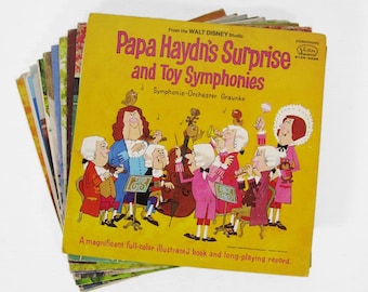 May include: A stack of vintage vinyl records. The top record has a yellow cover with the title "Papa Haydn's Surprise and Toy Symphonies" and illustrations of cartoon musicians. The text "From the Walt Disney Studio" is also visible.